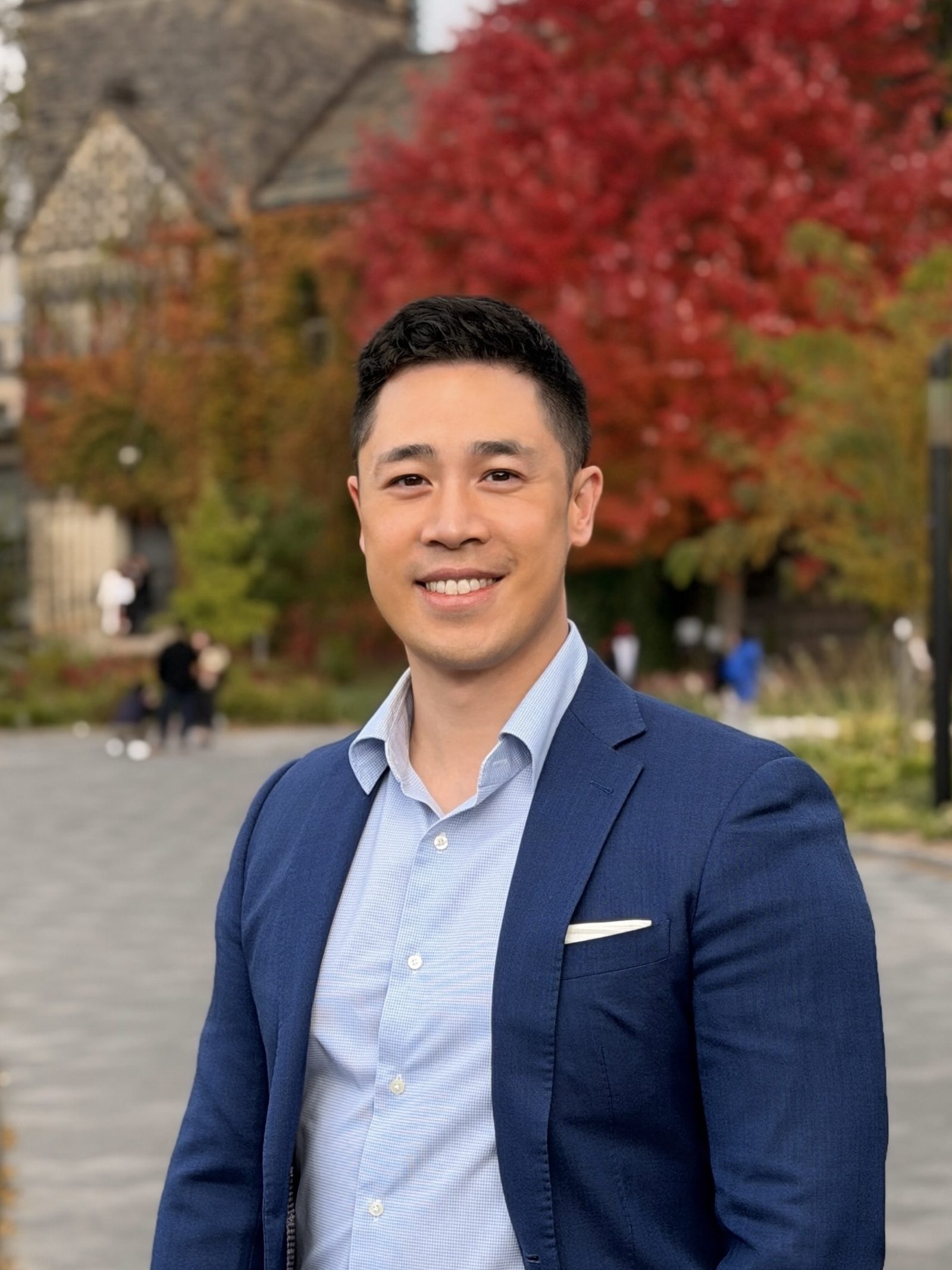 Victor Wong on a campus path in autumn, a vivid red and orange maple tree behind him.